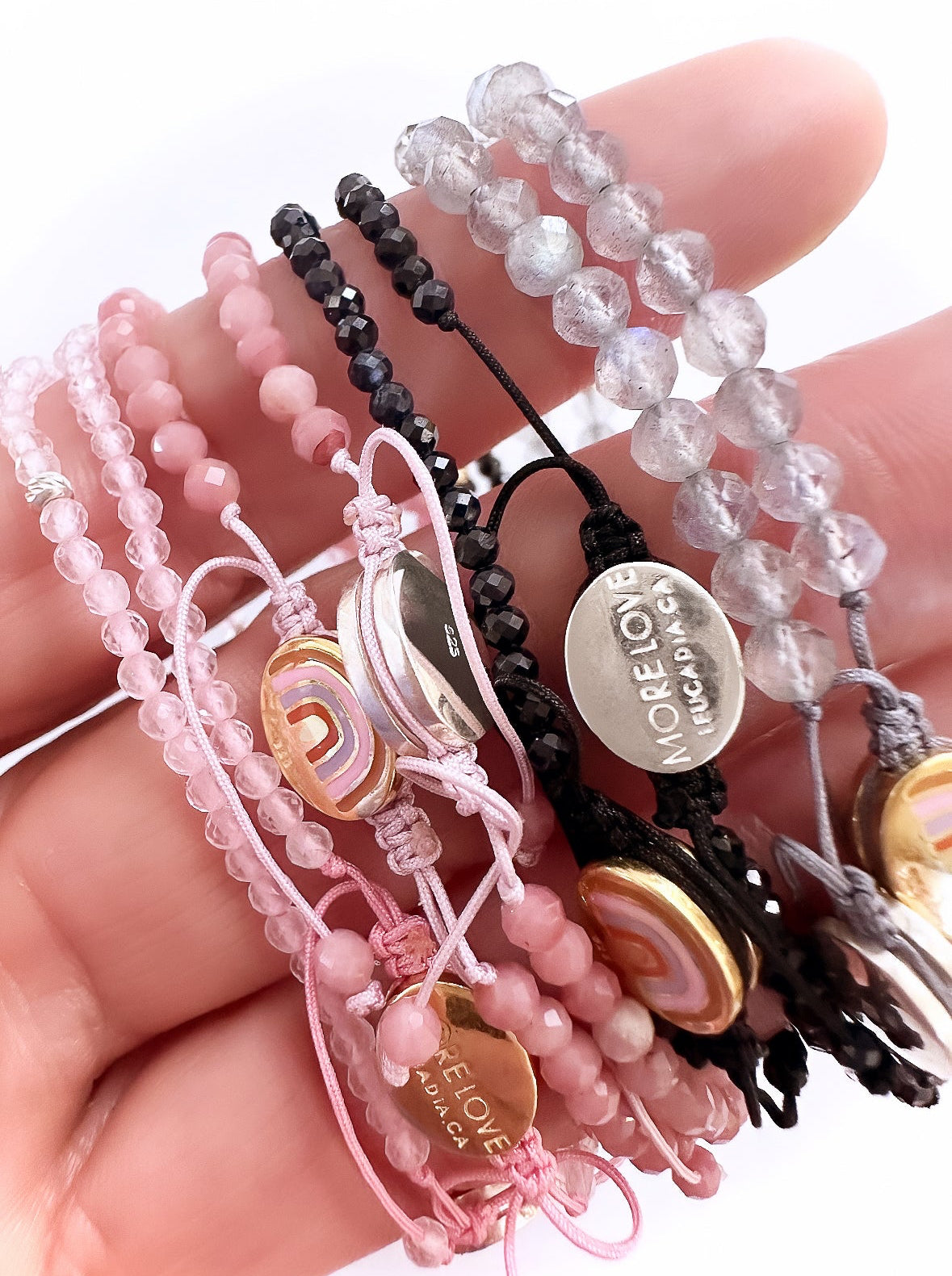 Hand holding More Love Community Bracelets. Bracelets are crystal and silver. Close up of More Love Bracelets.